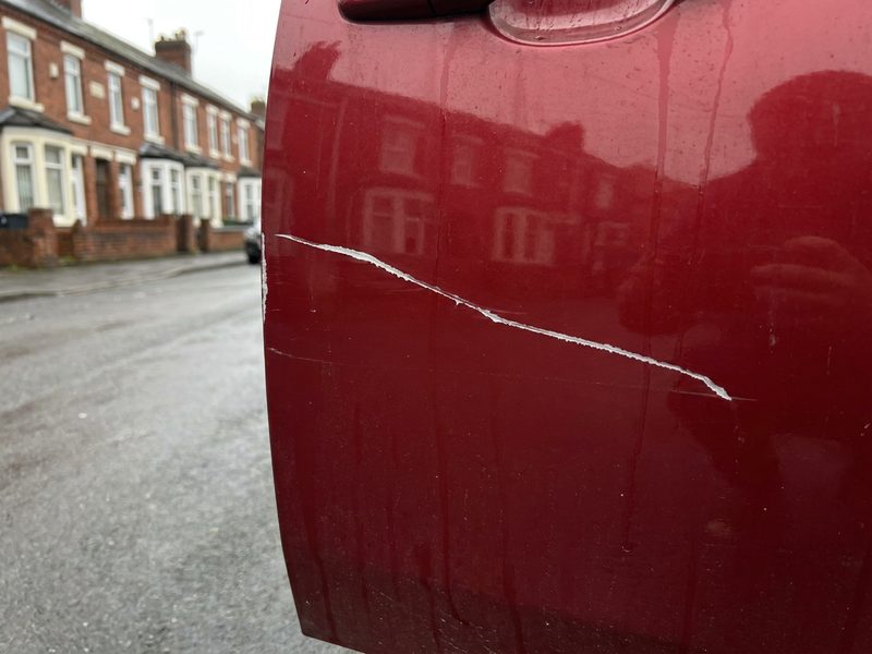 Scratched red door panel before repair